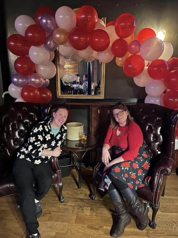 Two people sitting infront of red and white balloons
