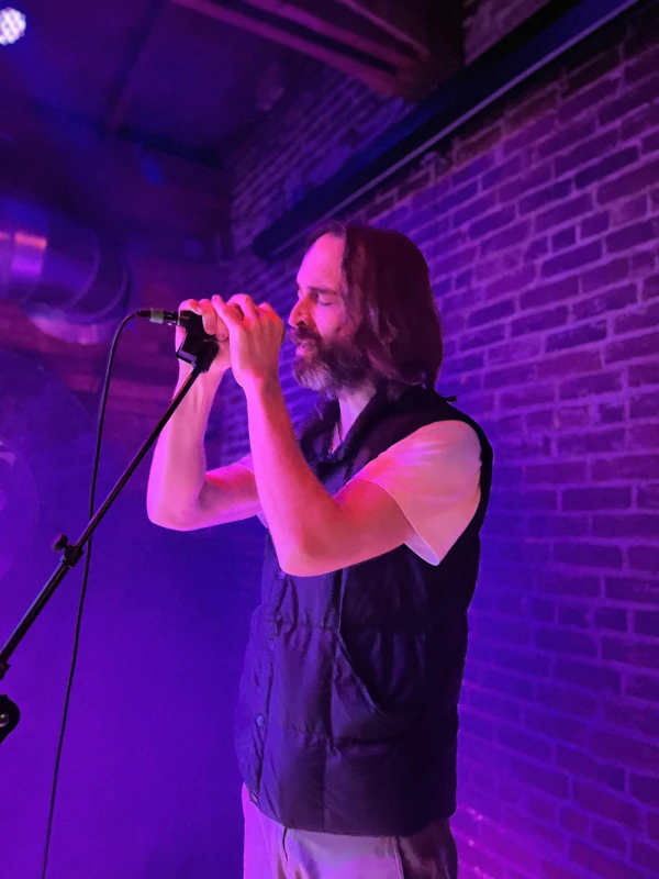 Man singing in front of a microphone on stage of Speakeasy