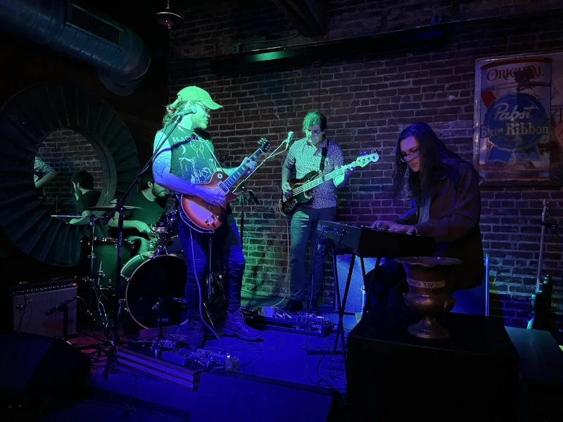 Band bathed in blue and green light playng on stage of Speakeasy in Carrboro